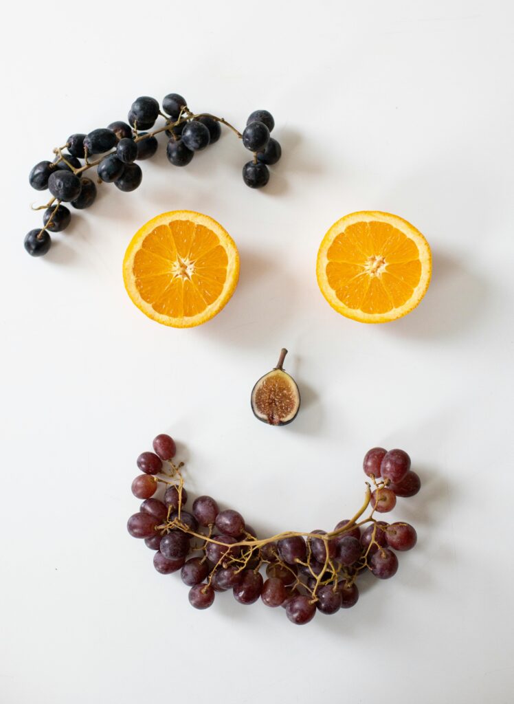 From above arrangement of fresh cut orange and ripe fig with bunches of grapes composed as smiling face with big eyes